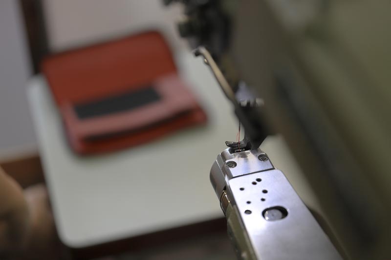 ミシンにフォーカスした画像。奥に縫製後のロングウォレットが見える